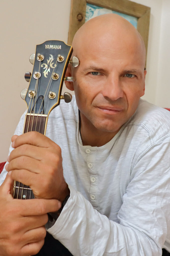 Cedric Vandenschrik looking towards camera with guitar next to him